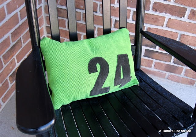 A  green pillow with the number 24 in black sits on a black chair on a front porch.