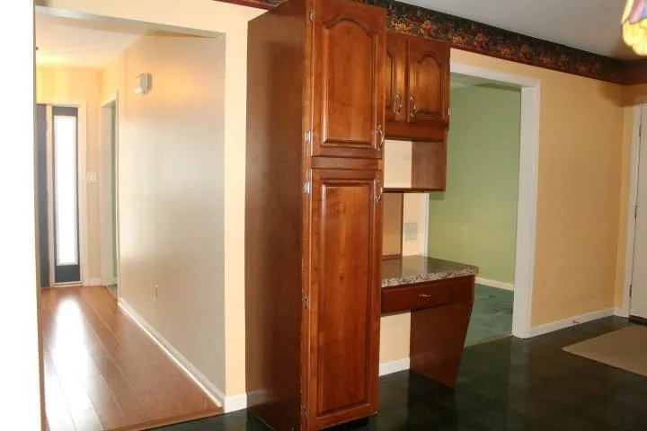 An outdated home with view of hallway, formal dining room, and built in desk and cabinets in a kitchen. The photo shows a before shot prior to a complete renovation and transformation.