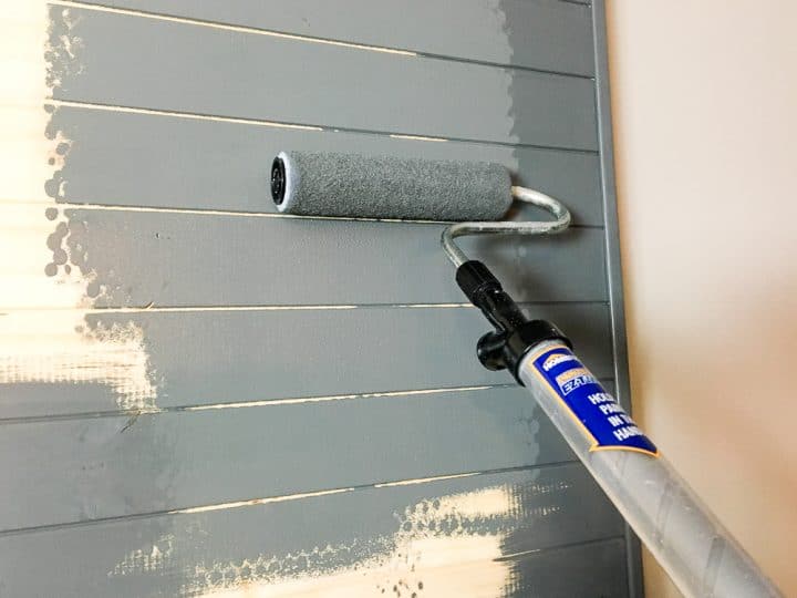 A paint roller brush painting a DIY wood accent tv wall in grey