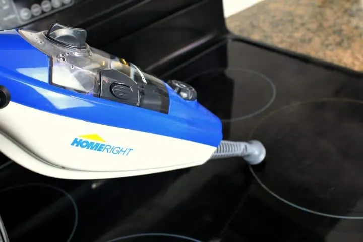 A handheld steam cleaning machine steaming a ceramic stove top