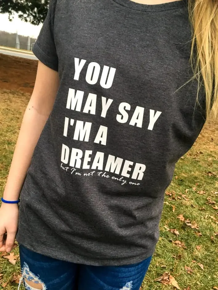 A girl wearing a dark great tshirt with the text "You May Say I'm a Dreamer but I'm Not the Only One" 