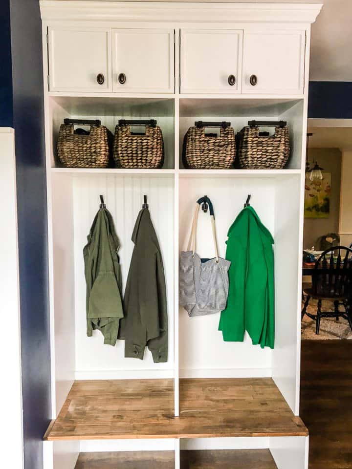 After shot showing a DIY mudroom coat bench with baskets and cubby organizers. Part of a tutorial about how to build and install a mudroom coat bench in your house.