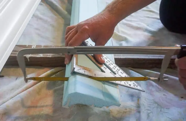 cutting a piece of foam crown molding with a hacksaw