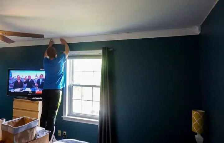 guy standing on a ladder holding a piece of crown molding in place