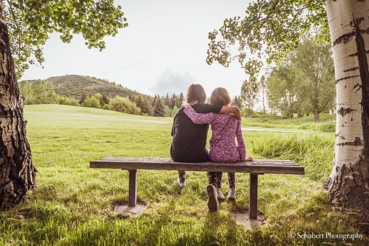 photo of the backs of two kids sitting on a bench in a field