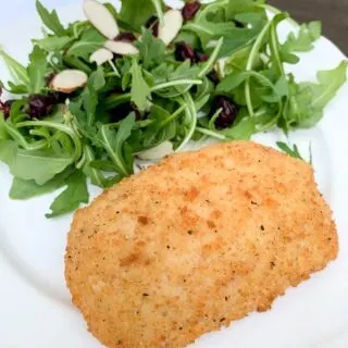 white plate with chicken cordon blue and a salad with cranberries and almond slices