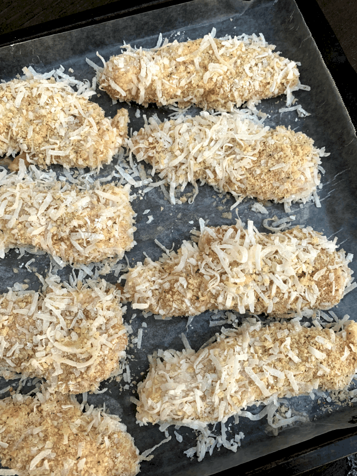 raw chicken tenders covered in shredded coconut and panko bread crumbs