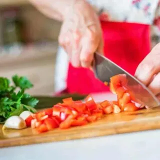 A female hand with a kitchen knife dicing tomatoes at home