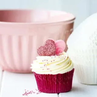an image of a homemade valentines themed cupcake and cupcake liners and a mixing bowl on a white wooden table