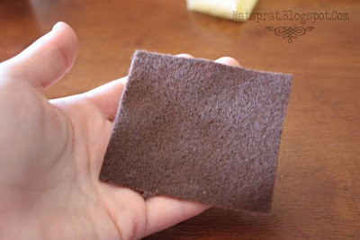 A hand holding a small square of grey felt