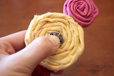 A detail shot showing a hand pressing a metal button into the center of a fabric rosette to embellish it
