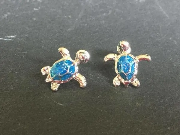 Silver stud turtle earrings with blue opal shells on a grey  countertop