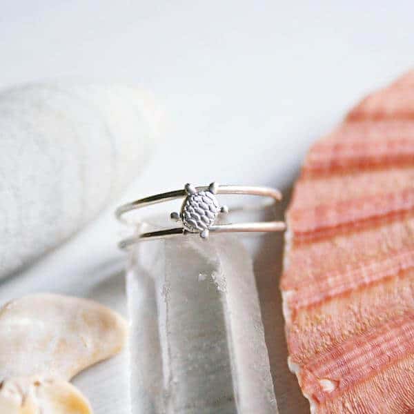 A small turtle silver ring with a double band is pictured against a white background with scattered seashells