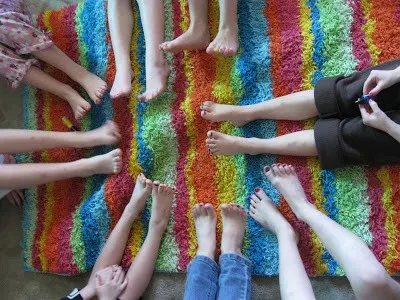 A birds eye photo of young girls' legs and feet together in a circle. Their toenails are painted different colors. 