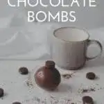 A pinterest pin with a photo of a hot chocolate bomb on a table with a mug and mini oreos and cocoa mix strewn about. The text says Hot Chocolate Bombs