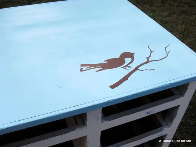 A brown bird on a branch is stencilled on a blue desk top