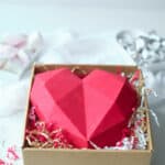 An edible chocolate box made from red candy melts sits in a box on a bed of shredded paper