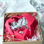 An edible chocolate box is cracked open to reveal wrapped Hershey's Kisses chocolates inside.
