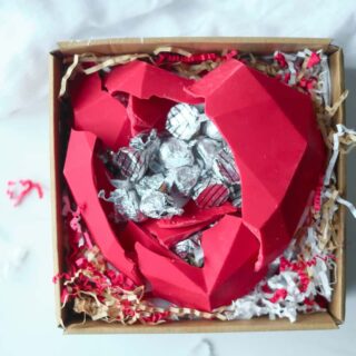 An edible chocolate box is cracked open to reveal wrapped Hershey's Kisses chocolates inside.