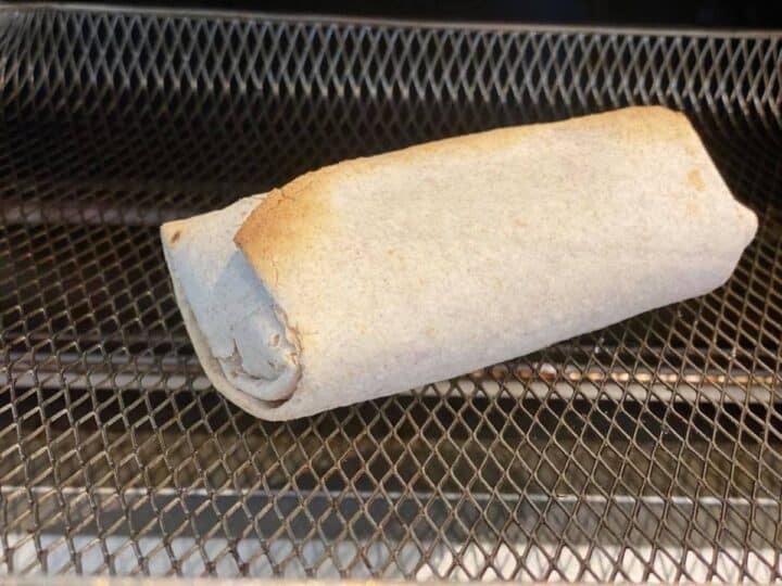 A frozen burrito in an air fryer basket after being cooked
