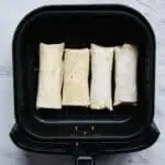 4 frozen burritos lining the basket of an air fryer