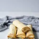 4 frozen burritos that have been cooked in an air fryer, stacked on a white plate.