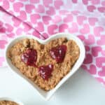 Chocolate oatmeal served in a heart shaped bowl and garnished with red jam hearts