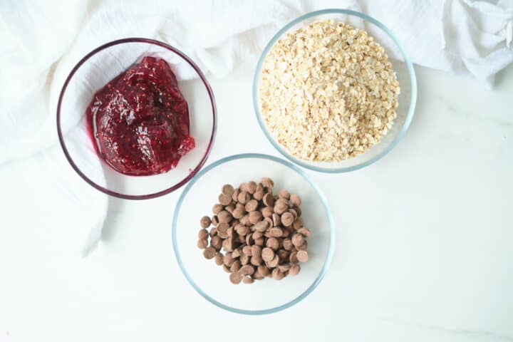Ingredients for a chocolate oatmeal Valentine's Day breakfast idea. Bowls of chocolate chips, oatmeal and jam on a table.