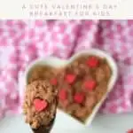 A Pinterest pin with an image of chocolate oatmeal on a spoon, garnished with a red candy heart. The full bowl of oatmeal is in the background in a heart shaped bowl. The text says Heart Shaped Chocolate Oatmeal. A Cute Valentine's Day Breakfast for Kids