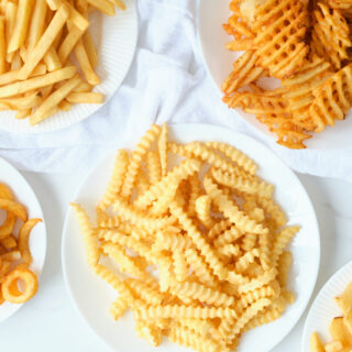 5 plates containing 5 different types of frozen fries after being cooked in an air fryer.