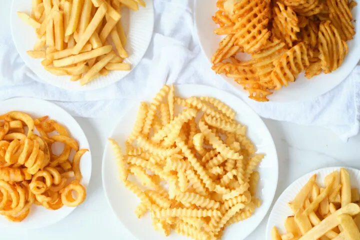 5 plates containing 5 different types of frozen fries after being cooked in an air fryer. 