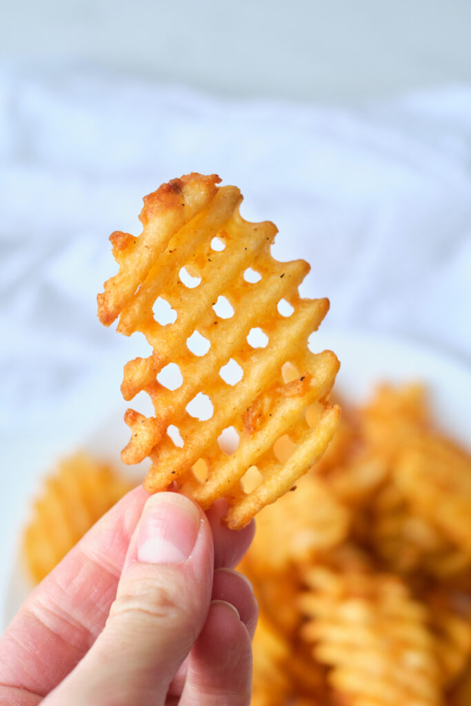 A woman's hand holds a waffle fry up close