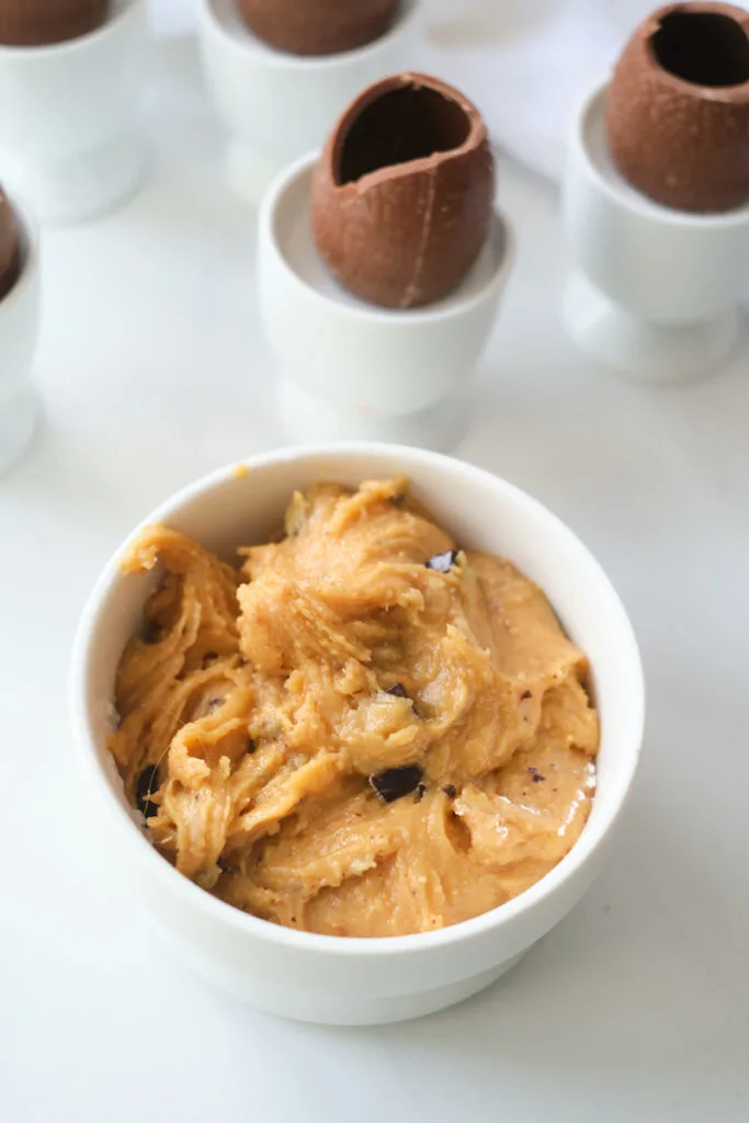 A dish of creamy peanut butter and chocolate chip mixture in front of hollow milk chocolate easter eggs sitting in egg cups