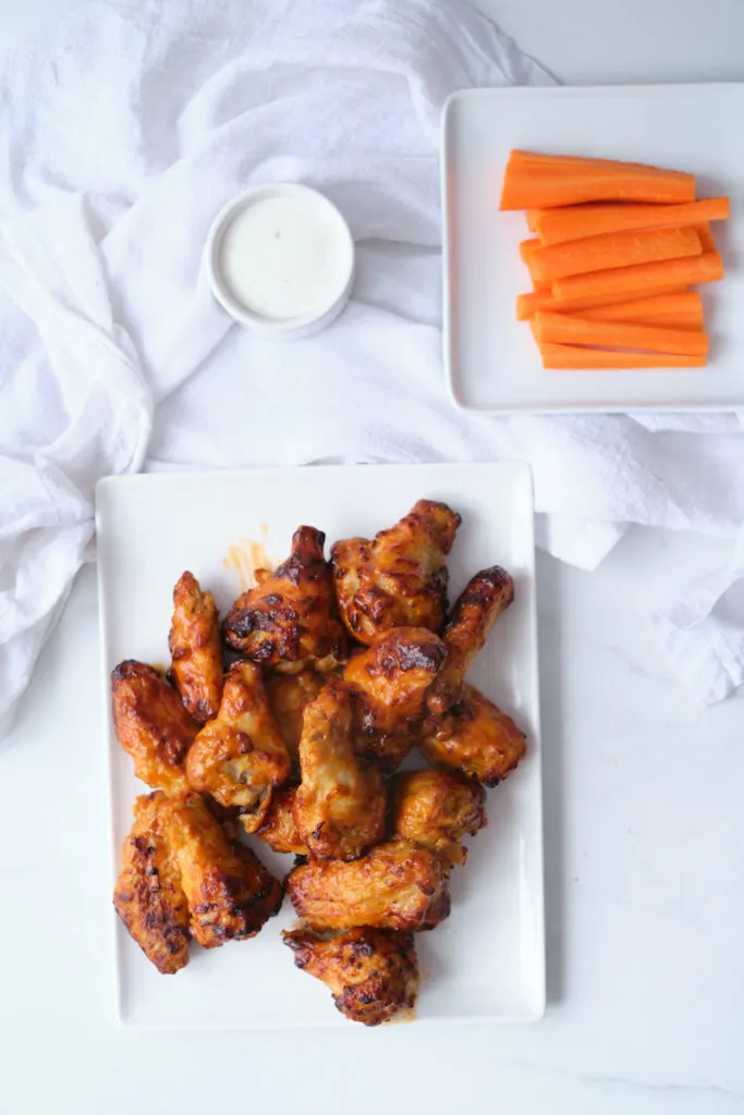 Air fried buffalo chicken wings on a plate with carrot sticks and dip in view