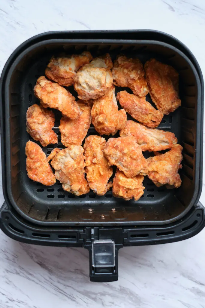Frozen chicken wings in air fryer basket before cooking