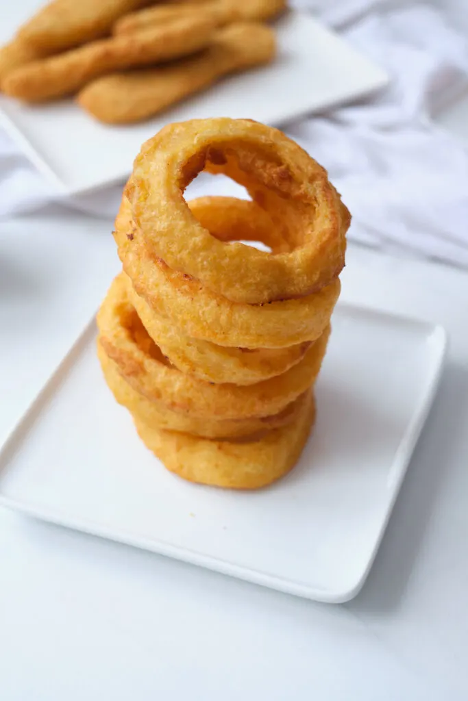 Stack of air fryer onion rings on a white dinner plate.