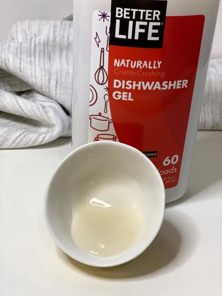 A bottle of Better Life dishwasher gel with a small dish containing the white gel in front