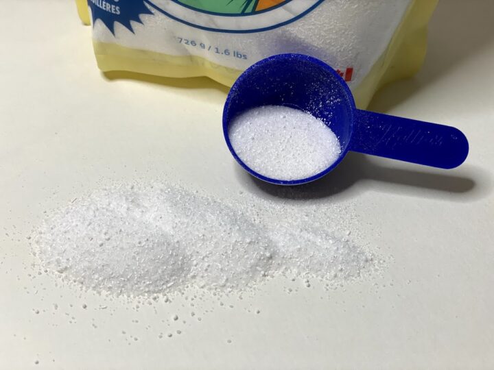 A scoop of Nellie's dishwasher powder with some of the powder spilled in front