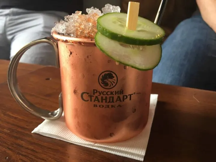 Close up of a moscow mule in a frosty copper mug piled high with crushed ice and garnished with cucumber